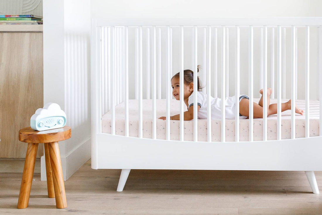 A baby lays in a bed listening to SNOObie white noise machine