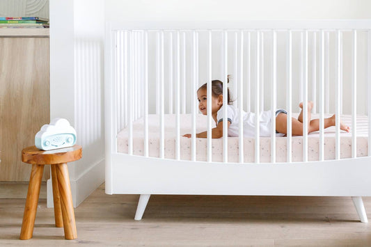 A baby lays in a bed listening to SNOObie white noise machine