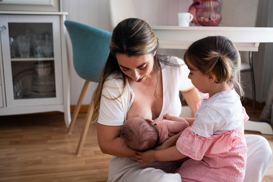A mum nurses her infant while her toddler sits nearby