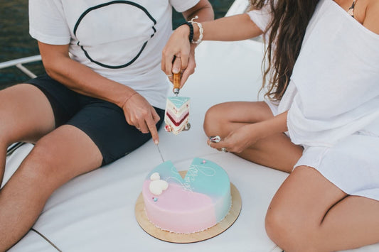 A couple slices into a pink and blue gender reveal cake to reveal pink fruit filling inside.